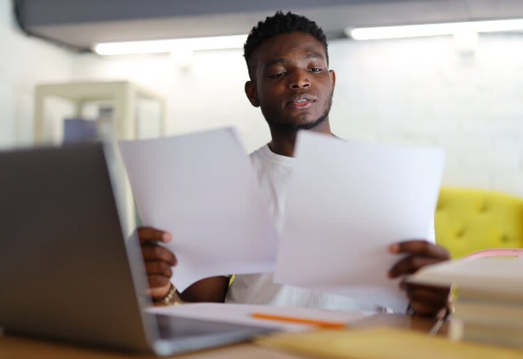 a man sitting in front of a laptop computer holding papers