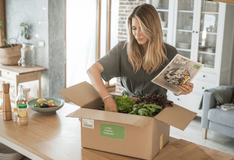 a woman opening a box of meal delivery on a table